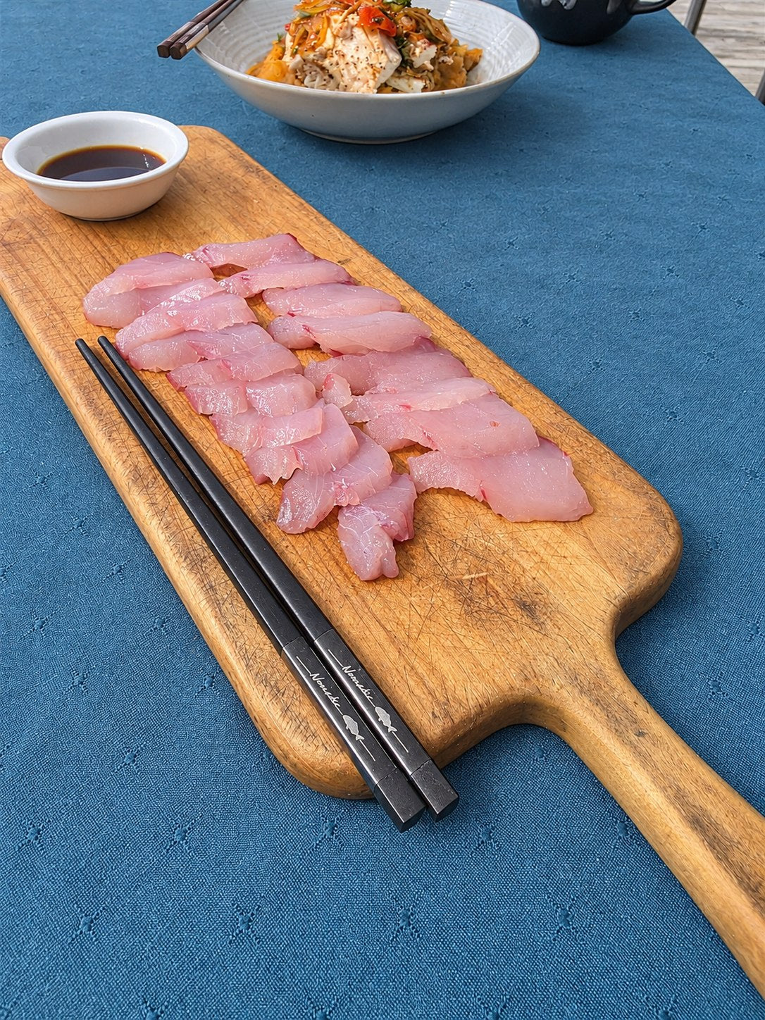 Nomad Chopsticks beside freshly prepared fish on a wooden board